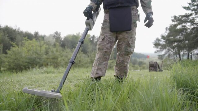Military sapper with a metal detector in the field. Ukrainian Explosive Ordnance Disposal Officer detecting metal by metal detector device. A man in a protective helmet and equipment
