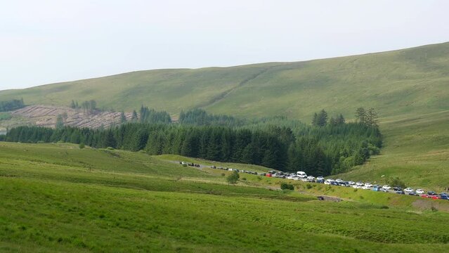 Handheld panning shot from hill of many vehicles parked on roadside of A470 road and in Pont ar Daf car park at the start of popular route to Pen y Fan peak in Brecon Beacons National Park in Wales.