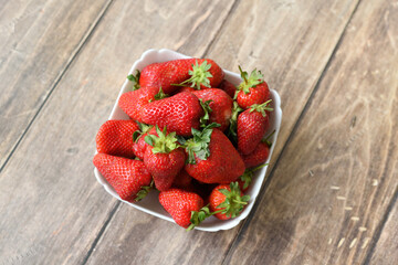 Ripe delicious strawberriesin a white plate on a wooden background