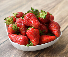 Ripe delicious strawberriesin a white plate on a wooden background