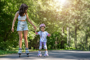 Mother teaching child daughter to skate on inline skates rollers in public park in summer. Family...