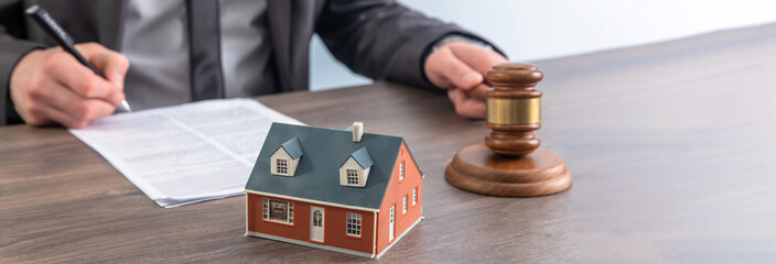 The hand of a judge with a gavel and a model of a house mediating property disputes in court