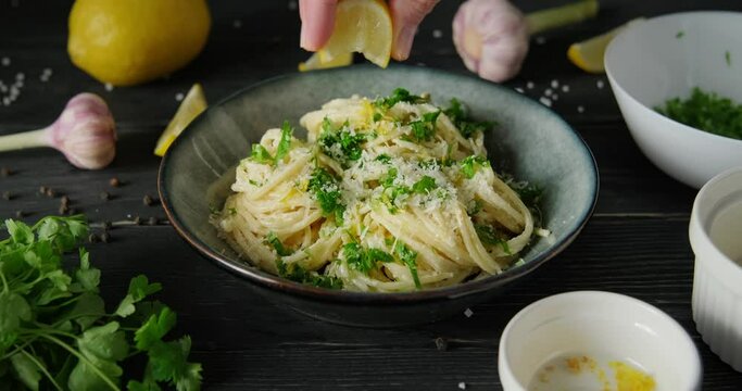 Preparing lemon pasta, hand squeezing lemon juice on spaghetti with white cream sauce, parmesan cheese and parsley, 4k footage, high quality horizontal video clip
