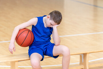 Sad disappointed boy with basketball ball in a physical education lesson
