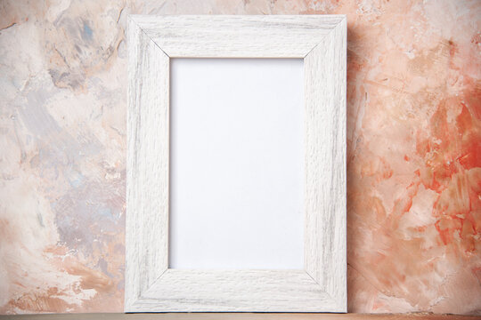 Close up view of empty white wooden photo frame hanging on nude colors wall with free space
