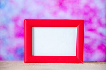 Close up view of red empty picture frame standing on white table on pastel colors background with free space
