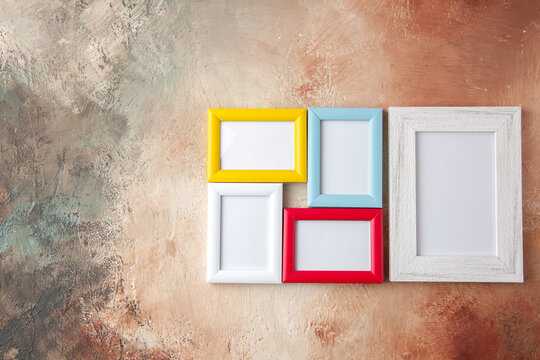 Close up view of small and big colorful picture frames hanging on nude color wall with free space