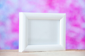 Close up view of white empty picture frame standing on table on pastel colors background with free space