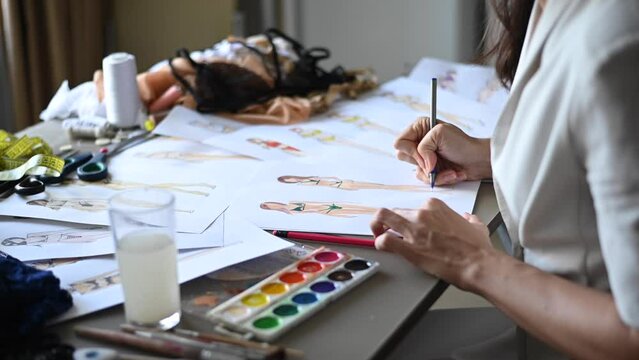 Faceless woman draws sketches of swimwear with a pencil. Close-up of the hands of a fashion designer.