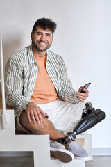 Happy young man with disability above knee transfemoral leg prosthesis sitting on stairs at home...