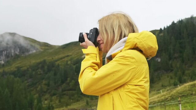 Blonde woman captures the beauty of the Alpine meadows through her camera lens. She wanders through the foggy hillsides, exploring the stunning scenery as a young tourist.