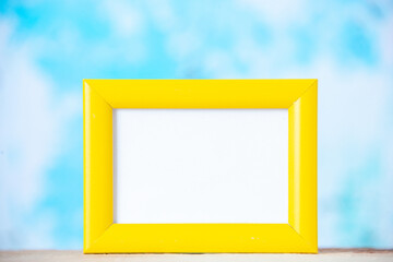 Close up view of yellow empty picture frame standing on white table on pastel blue background with free space