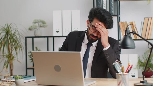 Indian businessman programmer software developer fingers crossed working on laptop loses becoming surprised by bad news results, fortune loss fail at home office. Deadline, bankruptcy. Freelancer man