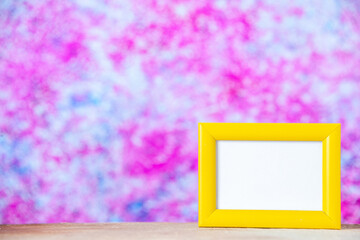 Front close view of yellow empty picture frame standing on white table on the left side on colorful background with free space