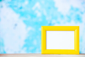 Front close view of yellow empty picture frame standing on white table on the left side on pastel blue background with free space