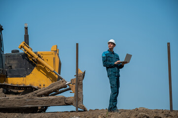 Caucasian male builder in hardhat holding laptop at construction site. 