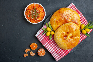 Overhead view of delicous fresh baked pastries kumquats with stem on red stripped towel and salad tangerines on dark blackground