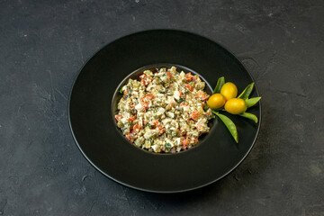 Side view of delicious salad served with kumquats with stem on a black plate on dark background