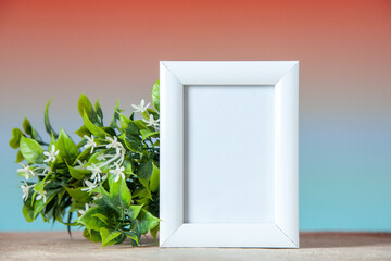 Top view of empty picture frame standing on table and flower pot on pastel peach blue colors background with free space