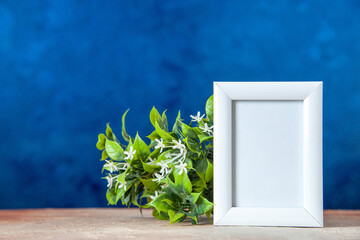 Top view of empty picture frame standing on table and flower pot on sky blue background