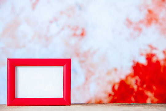 Top view of red empty picture frame standing on the right side on white table on red white mix background with free space