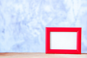 Top view of red empty picture frame standing on white table on the left side on blue ice background with free space