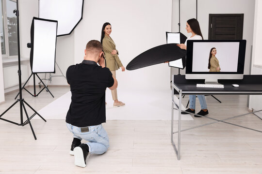 Professional photographer and assistant working with beautiful model in modern photo studio