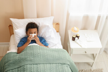 African-American boy with scarf and tissue blowing nose in bed indoors, above view. Cold symptoms