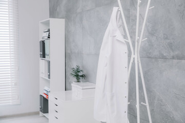 White doctor's gown hanging on rack in clinic. Space for text