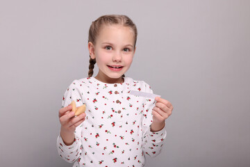 Cute girl holding tasty fortune cookie and reading prediction on light grey background