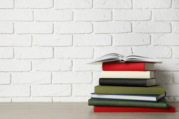 Fototapeta na wymiar Stack of hardcover books on grey table near white brick wall, space for text