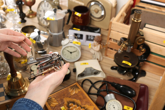 Woman holding bunch of old keys near table with different stuff, closeup. Garage sale