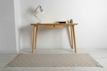 Stylish lamp, books and houseplant on wooden table in light room. Interior design