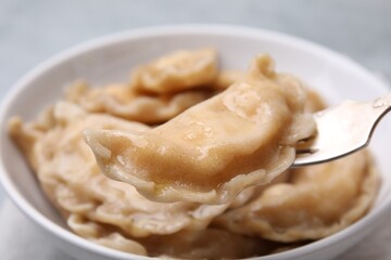 Delicious dumpling (varenyk) with cottage cheese on fork over bowl, closeup