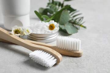 Fototapeta na wymiar Bamboo toothbrushes, flowers and sea salt on light grey table, closeup