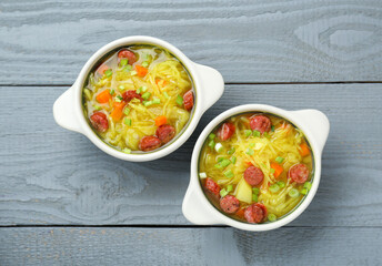 Delicious sauerkraut soup with smoked sausages and green onion on grey wooden table, flat lay