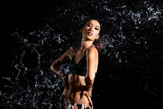 Tanned skin Asian woman in bikini poses in aqua studio. Splash Drops of water spread to body. Fun emotion female girl on water attack fluttering and stop motion freeze shot, black background isolated