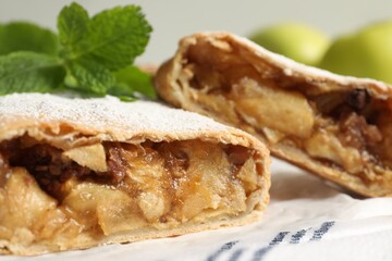 Delicious strudel with apples, nuts and powdered sugar on table, closeup