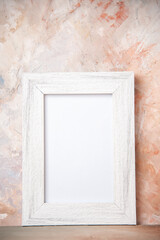 Vertical view of empty white wooden photo frame hanging on nude colors wall with free space