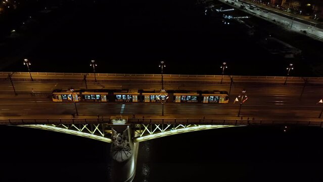 Aerial view of Budapest Margaret Bridge or Margit hid over River Danube, embankment at night. Public transport in the city. Yellow tram passing through the bridge