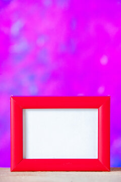 Vertical view of red empty picture frame standing on white table on blue abstract mixed paint background with free space