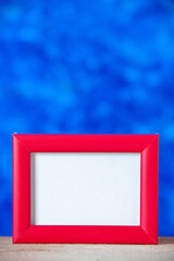 Vertical view of red empty picture frame standing on white table on light blue ice abstract background with free space