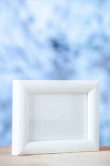 Vertical view of white empty picture frame standing on table on light icy background with free space