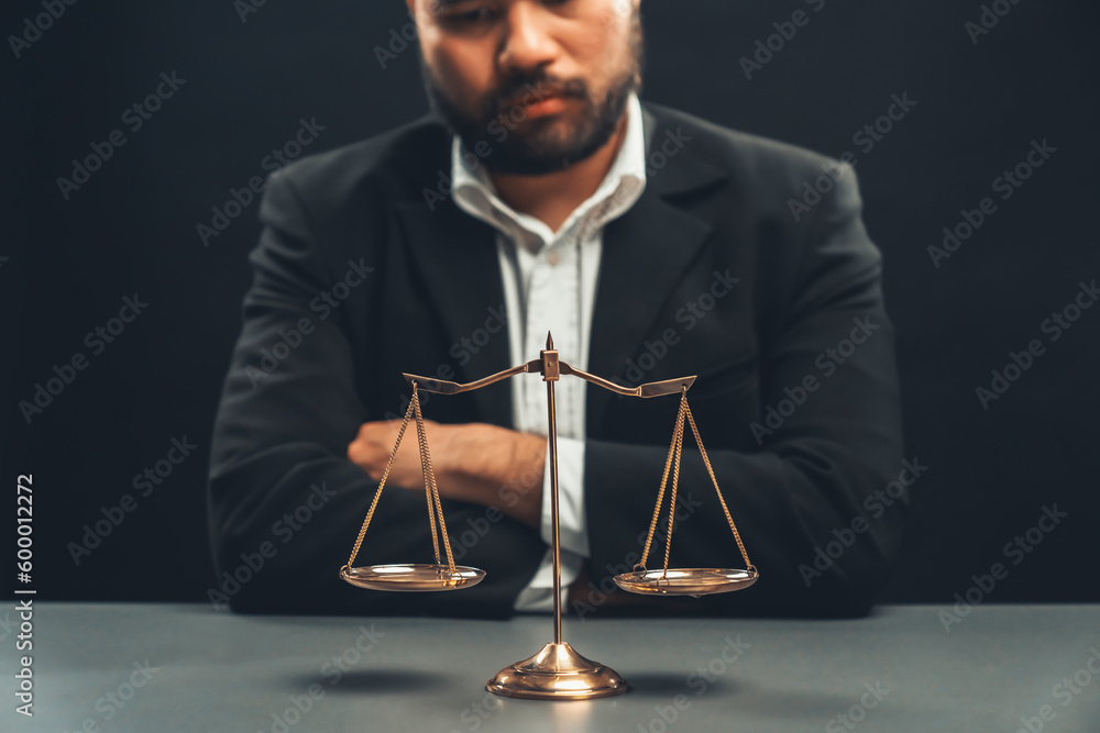 Poster focus golden scale balance with burred background of lawyer in black suit sit on his office desk, sy