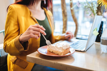 Professional digital nomad woman enjoying lemon pie while working remotely at a cafe in a yellow...