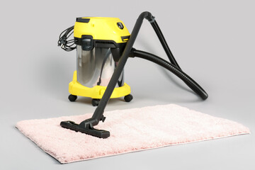 Vacuum cleaner with carpet on grey background