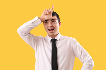 Young businessman showing loser gesture on yellow background