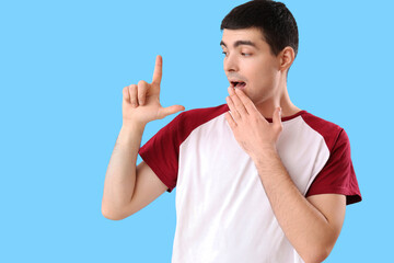 Shocked young man showing loser gesture on blue background