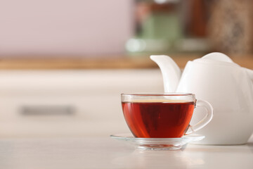 Cup of delicious tea and teapot on table in kitchen