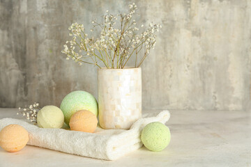 Vase with flowers, bath bombs and towel on table near grunge wall